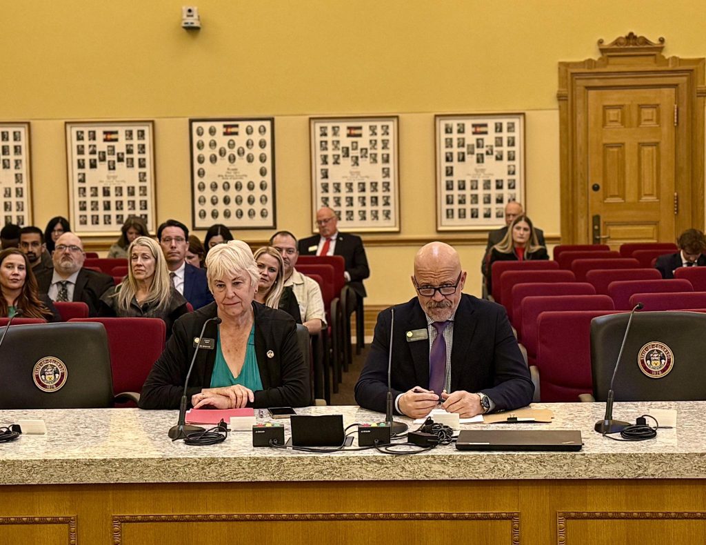 
Senator Scott Bright seated at a committee hearing table inside the Colorado State Capitol, prepared to testify before a Senate committee in Denver.