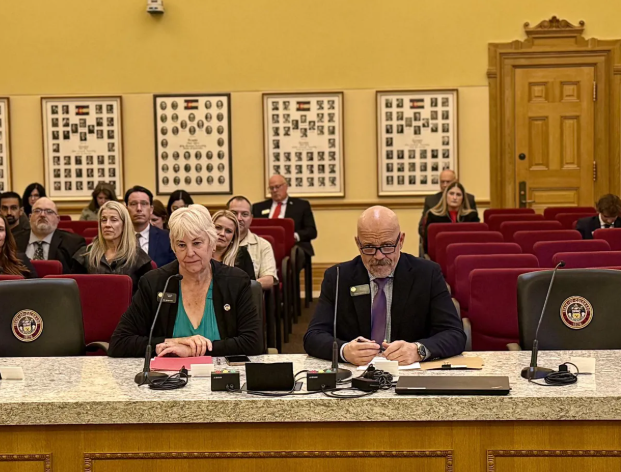 Senator Scott Bright seated at a committee hearing table inside the Colorado State Capitol, prepared to testify before a Senate committee in Denver.