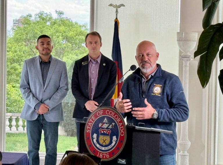 Senator Scott Bright speaking at a Colorado State Senate podium alongside community leaders and supporters at a District 13 event.